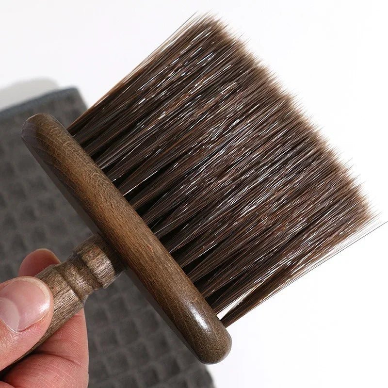 Hand holding a brush with brown bristles and wooden handle against a white background