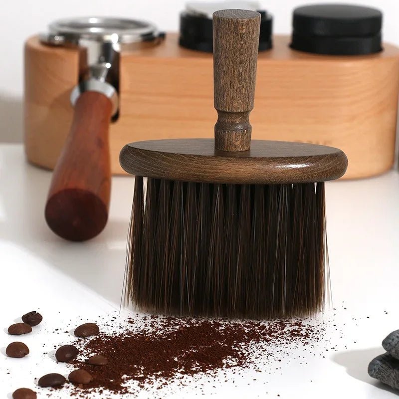 Wooden coffee brush with coffee beans and grounds on a white surface