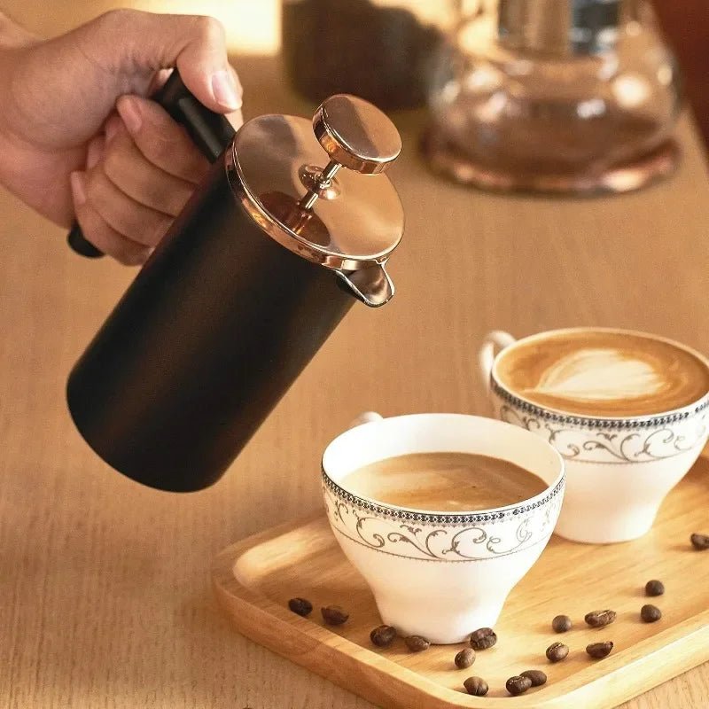 Person pouring coffee from a French press into two cups on a wooden surface with coffee beans.