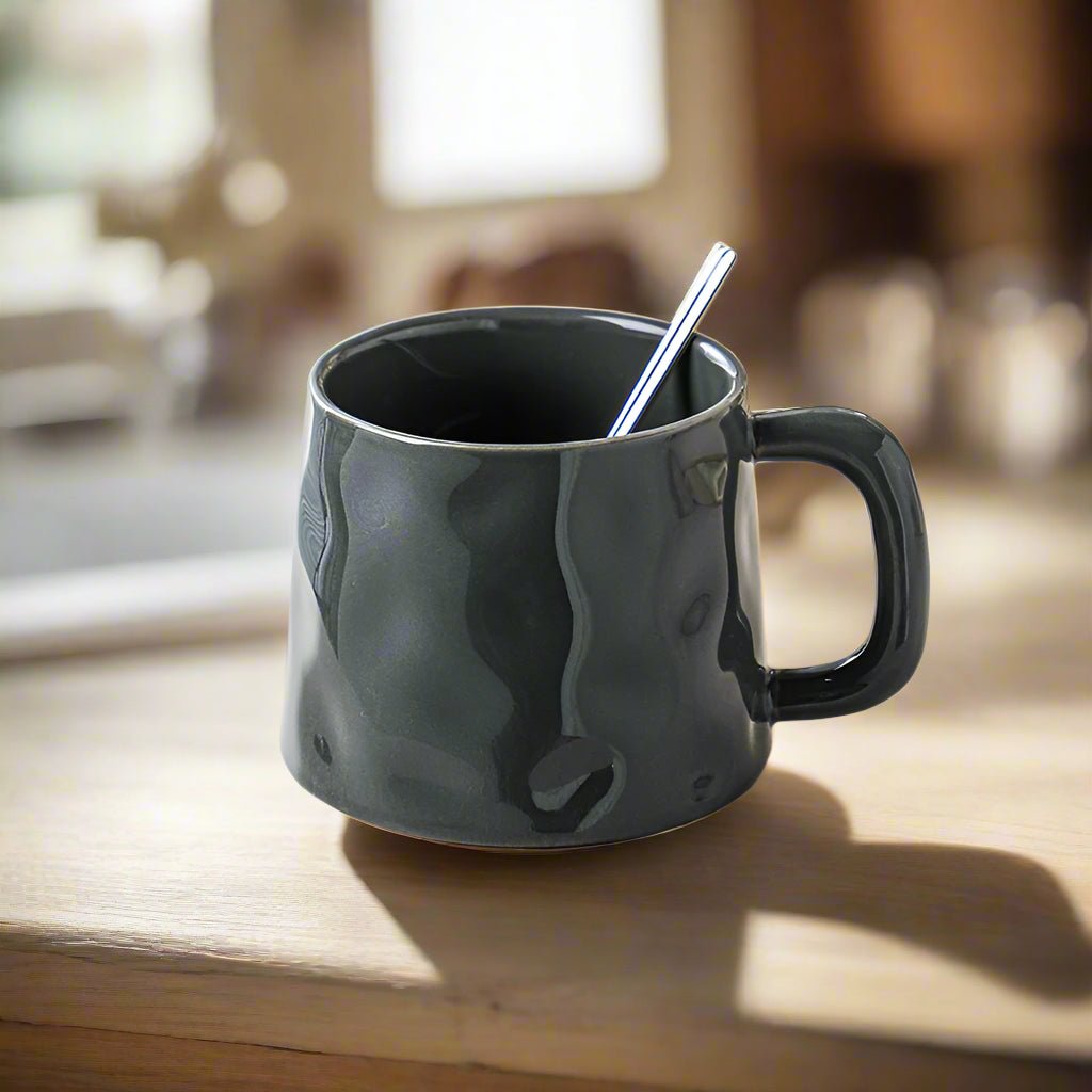 Black mug with a spoon on a wooden surface, blurred indoor background
