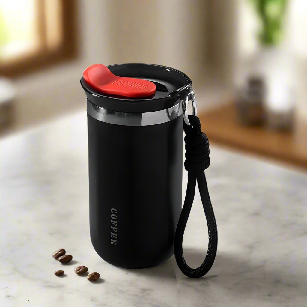 Black coffee tumbler with red lid and black rope handle on a marble surface.
