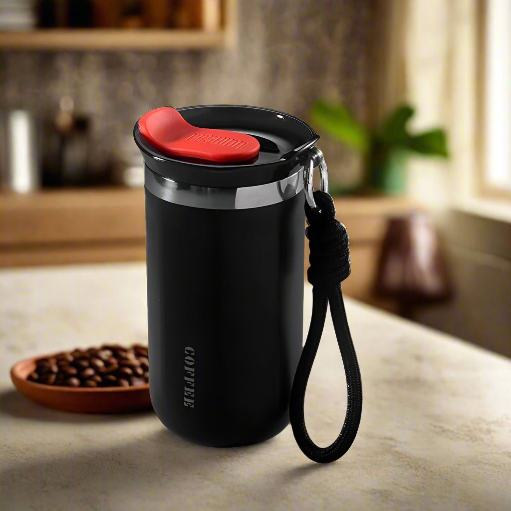 Black coffee tumbler with red lid on a kitchen counter