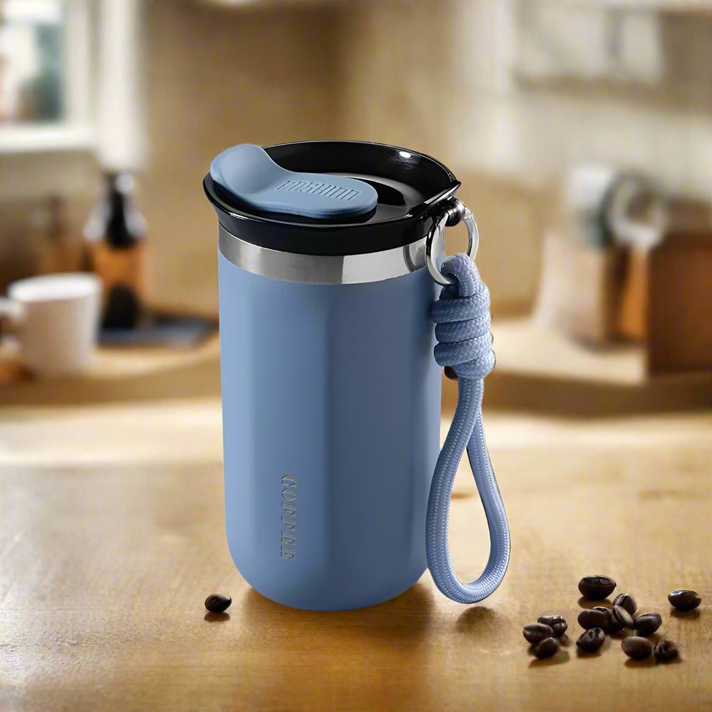 Blue tumbler with a black lid on a wooden surface with coffee beans.