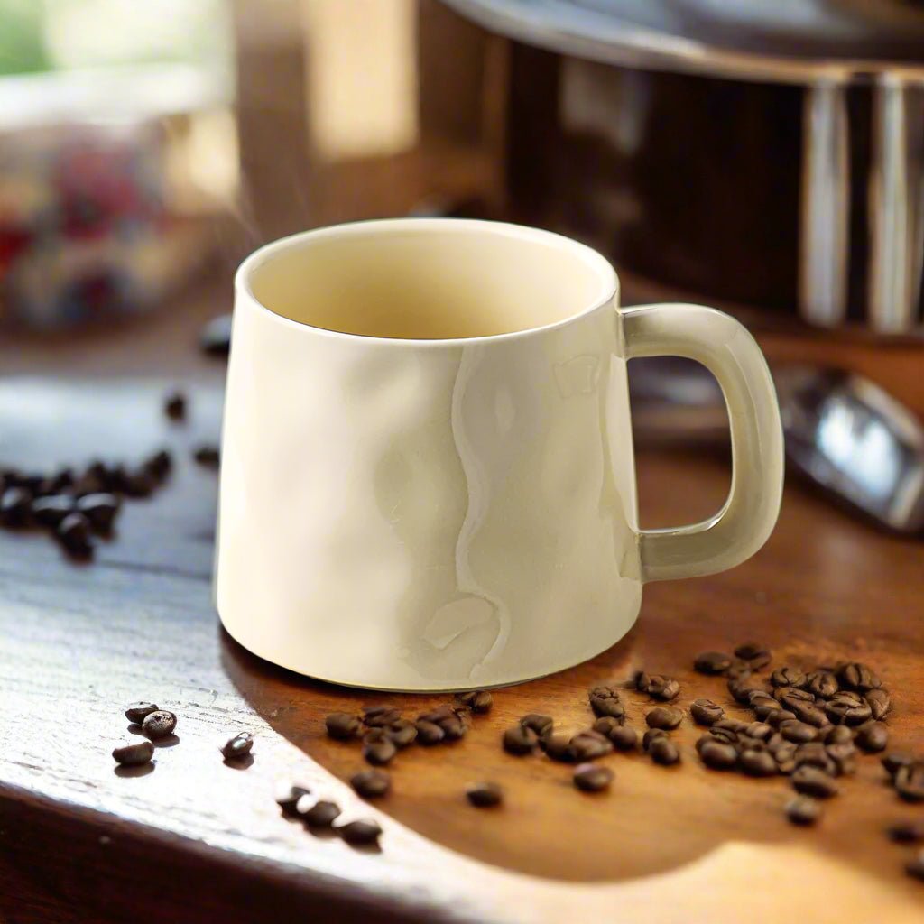beige ceramic mug with coffee bean design on a wooden surface with scattered coffee beans.