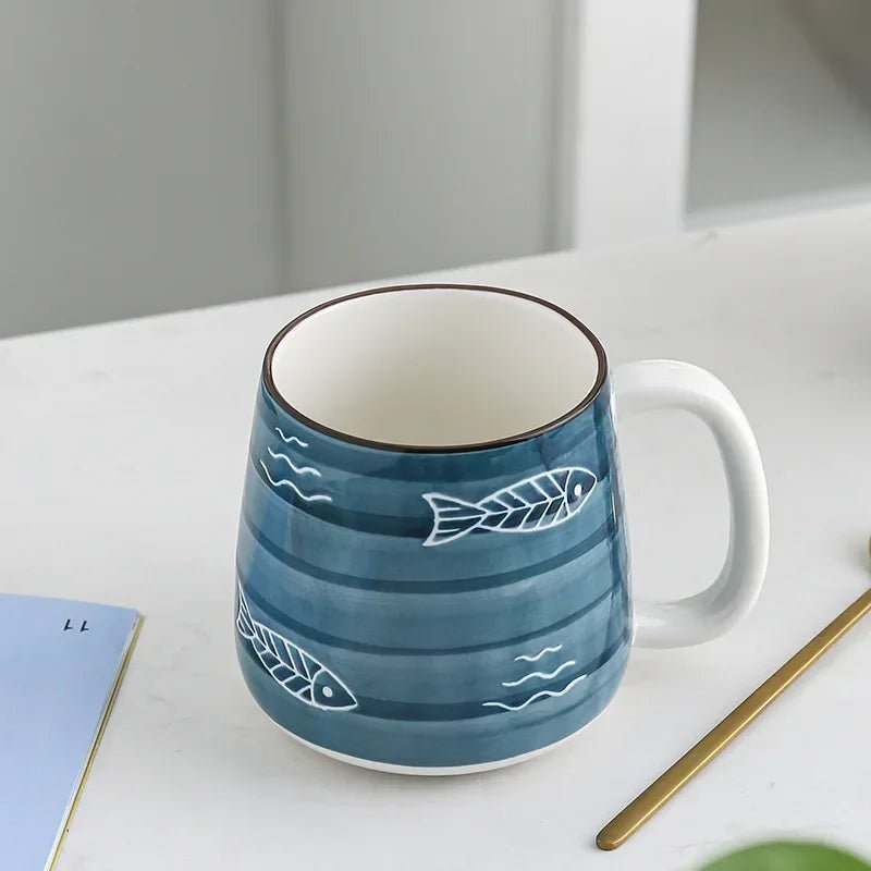 Blue ceramic mug with fish and wave patterns on a white surface