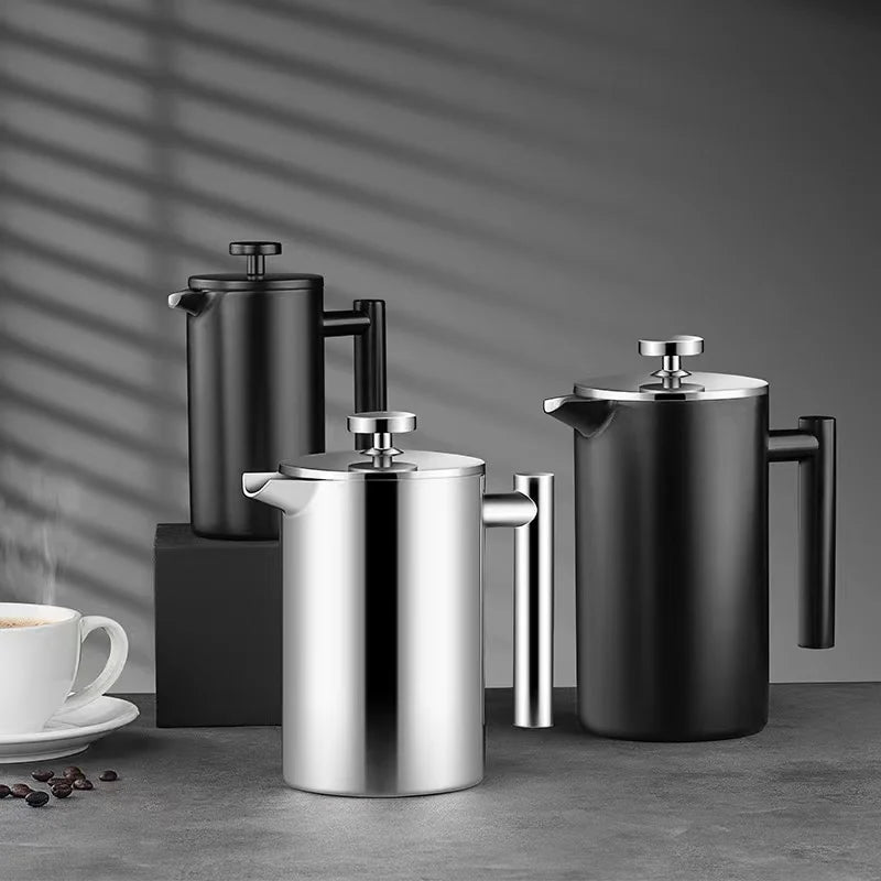 Three coffee presses in black and silver on a gray surface with a cup and saucer in the background.