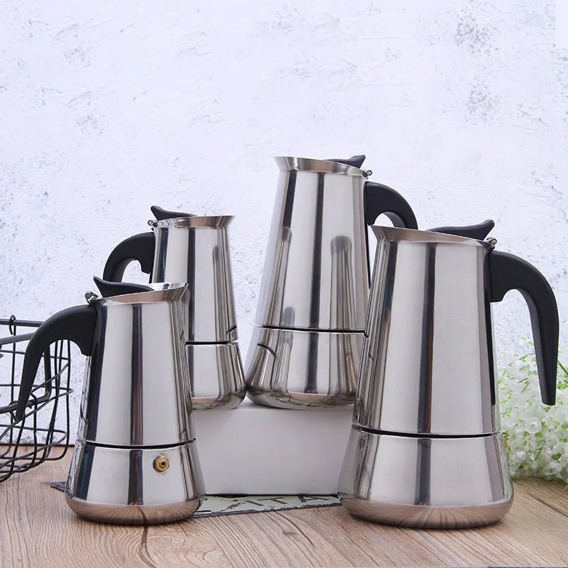 Set of four stainless steel espresso pots on a wooden surface with a light gray textured wall background.