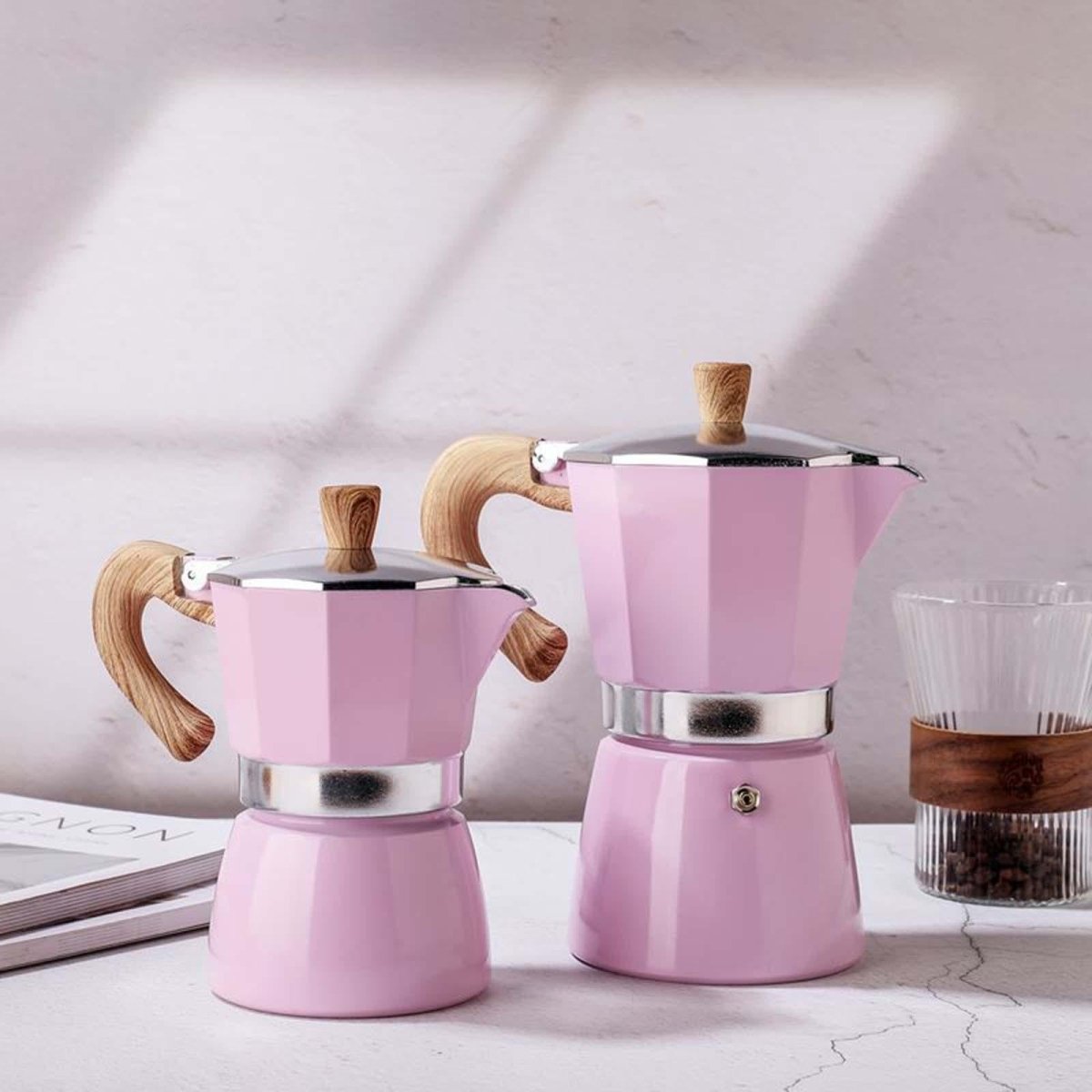 Two pink espresso pots with wooden handles on a light surface.