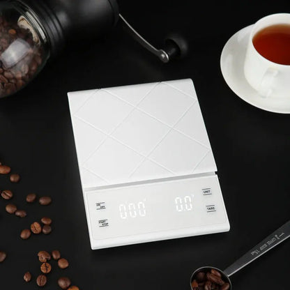 White digital kitchen scale on a dark surface with coffee beans and a cup of tea.