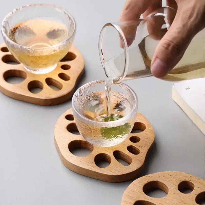 Person pouring tea into a glass cup on wooden coasters.