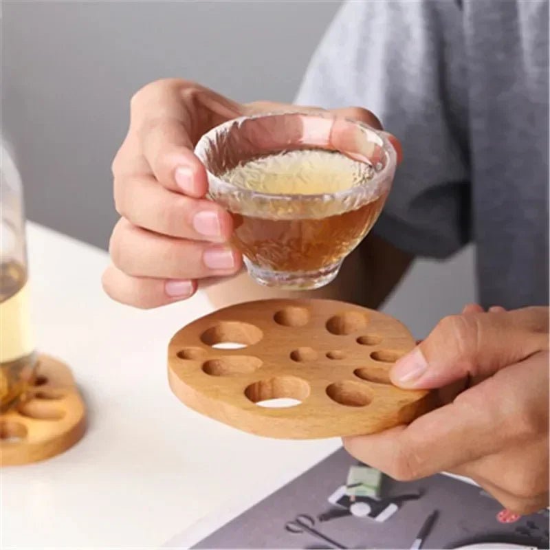 Person holding a small glass of tea with a wooden coaster on a table.