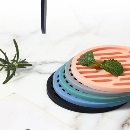 Set of silicone coasters in various colors on a marble surface with a plant.