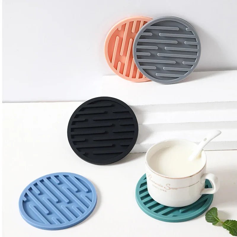 Set of silicone coasters in various colors on a white surface with a cup and spoon.