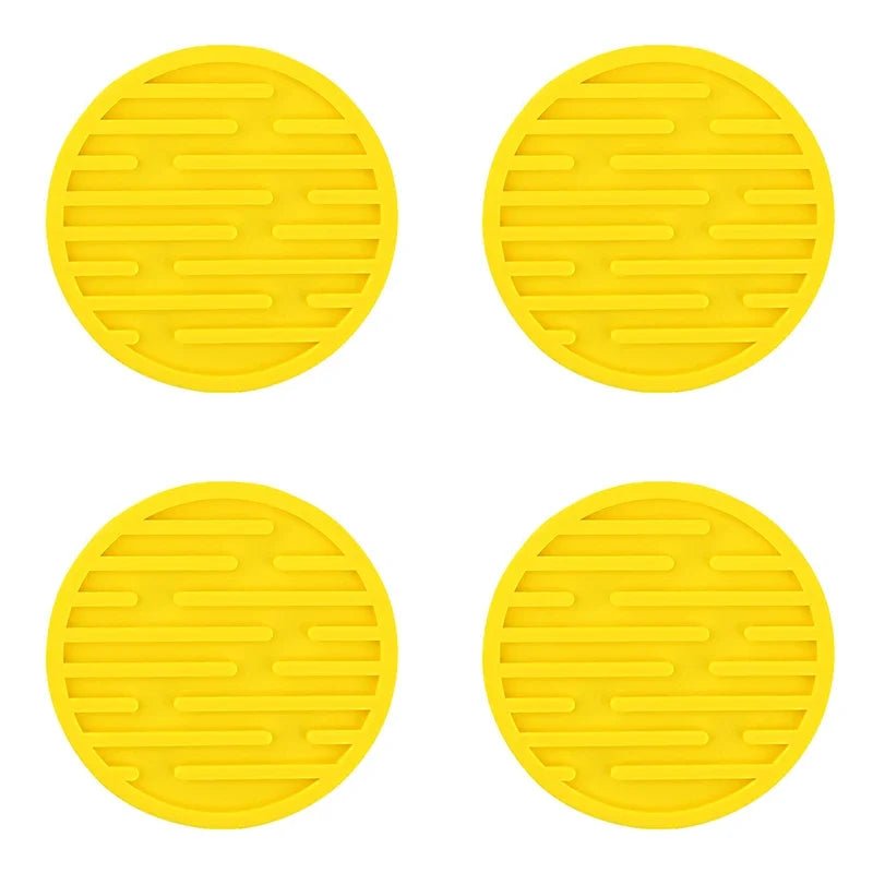 Four yellow silicone coasters with textured surface on a white background