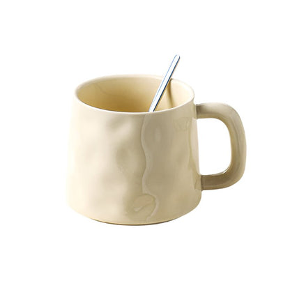 Beige mug with a handle and a spoon on a white background