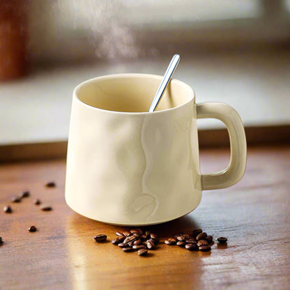 Beige mug with steam, spoon, and coffee beans on a wooden surface