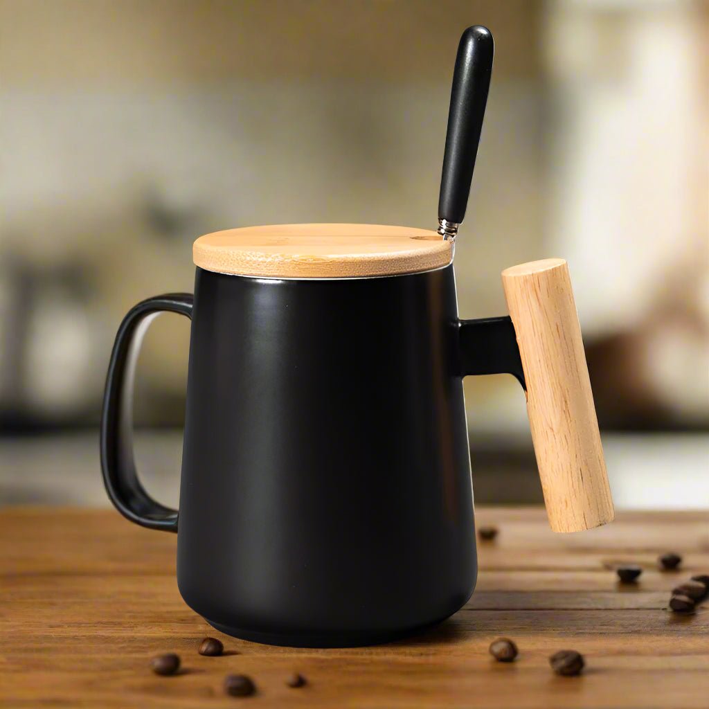 Black mug with wooden handle and lid on a wooden surface with coffee beans.
