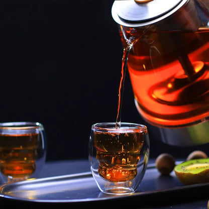 Tea being poured from a teapot into a glass cup on a dark background