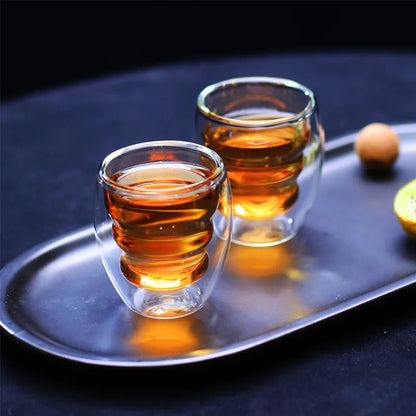 Two clear glass cups filled with a amber liquid on a dark surface.