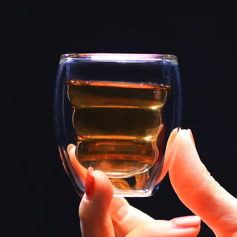 Hand holding a clear glass with layered liquid against a black background