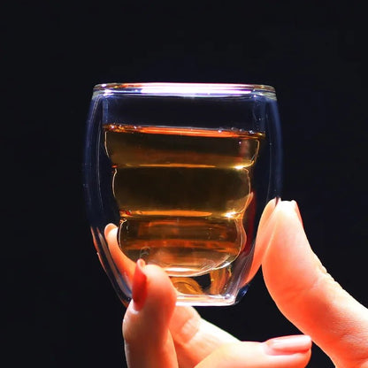 Hand holding a clear glass with layered liquid against a black background