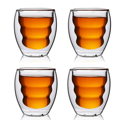 Four double-walled glass cups with a clear liquid on a white background