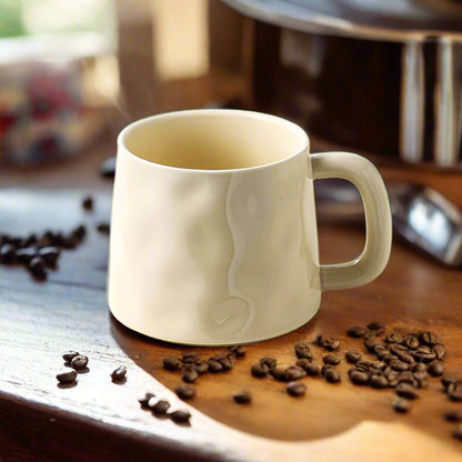 beige ceramic mug with coffee bean design on a wooden surface with scattered coffee beans.