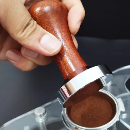 Hand using a wooden tamp to compress coffee grounds in a portafilter.