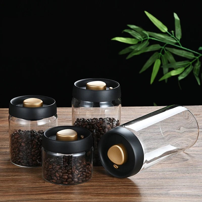 Set of glass jars with black lids and gold knobs on a wooden surface with a dark background and green leaves.