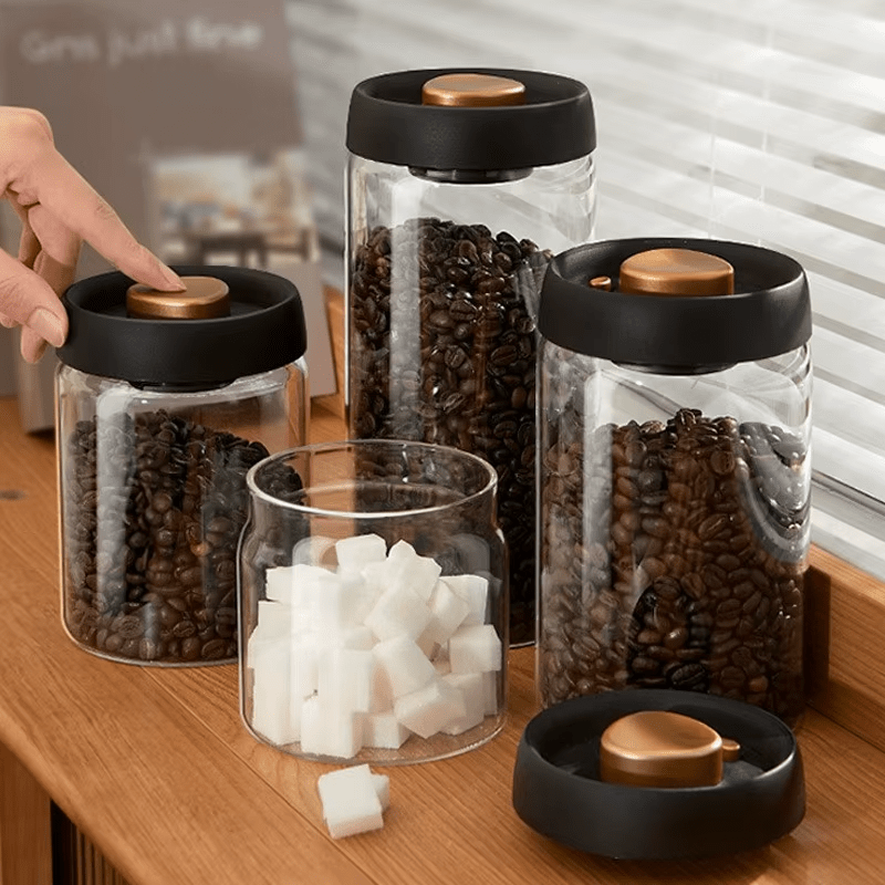 Glass jars with black lids containing coffee beans and sugar on a wooden surface.