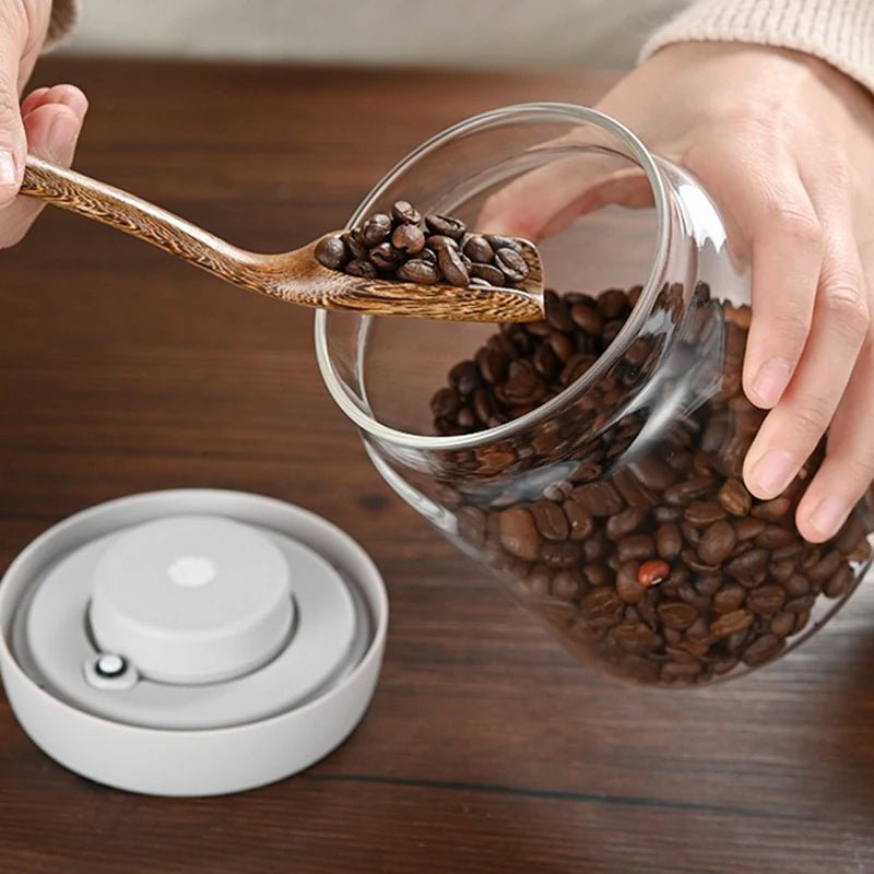 Glass container with coffee beans and a wooden spoon on a wooden surface