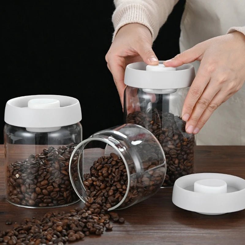 Person interacting with glass jars filled with coffee beans on a wooden surface.