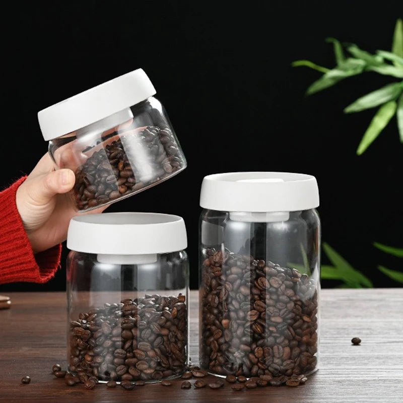 Three clear jars with white lids containing coffee beans on a wooden surface with a dark background.