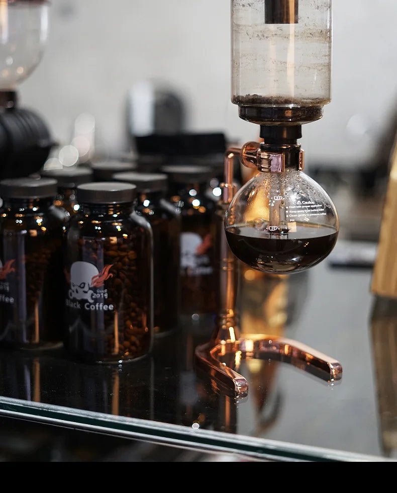 Coffee brewing process with a siphon coffee maker and coffee beans on a reflective surface.