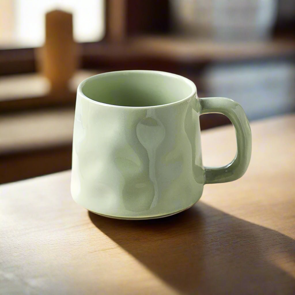 Light green ceramic mug on a wooden surface with a blurred indoor background