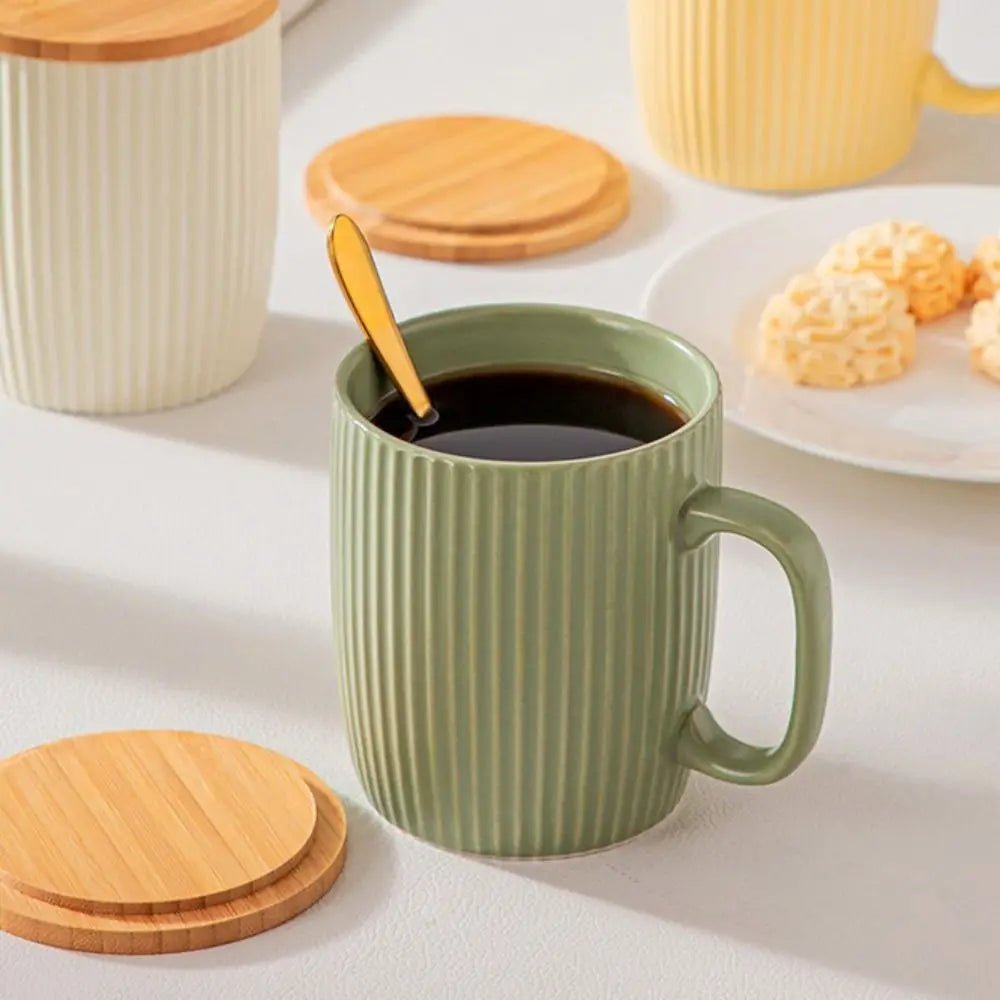 Green mug with striped pattern filled with coffee, surrounded by wooden coasters and a plate of cookies on a light background.