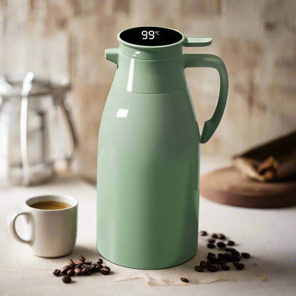 Green thermal coffee carafe with digital temperature display on a kitchen counter with coffee beans and a cup.