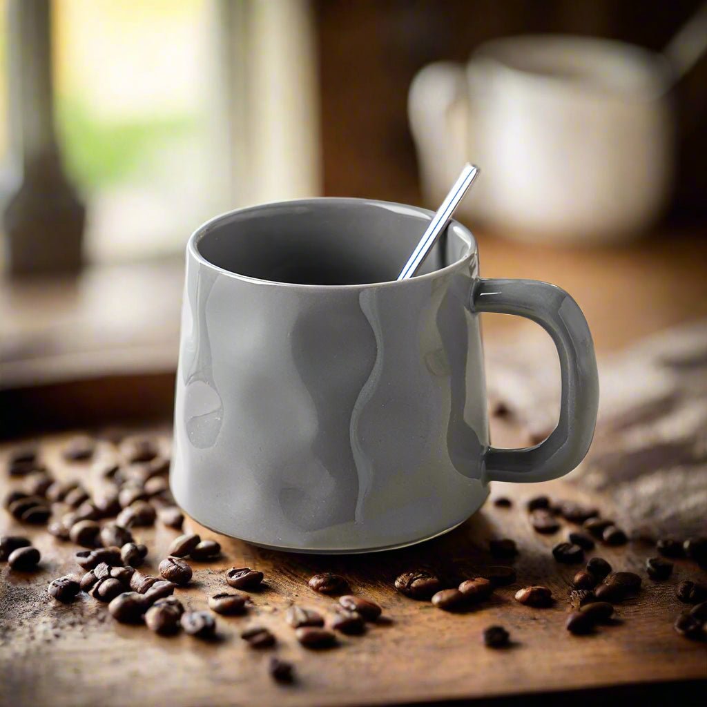 Gray mug with a spoon on a wooden surface with coffee beans