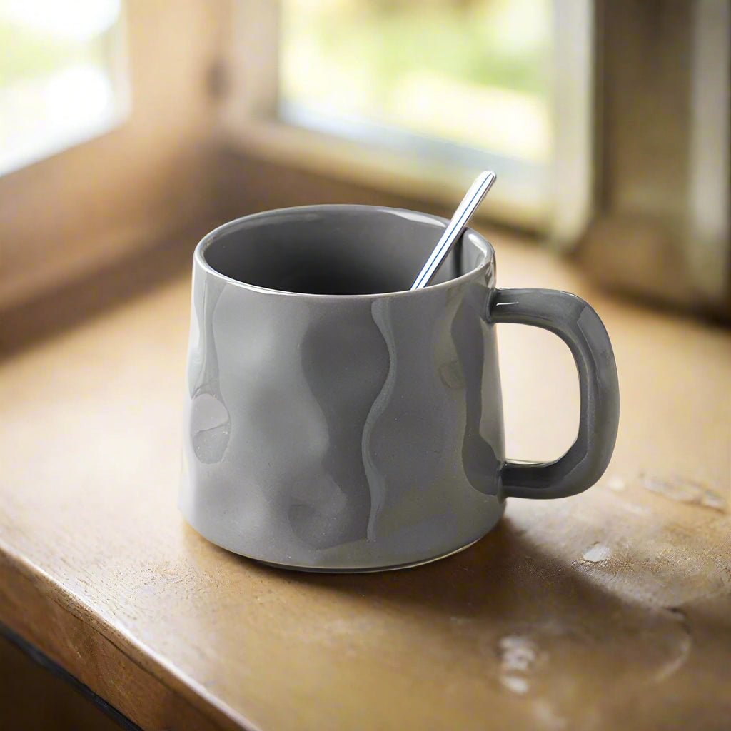 Gray mug with a spoon on a wooden surface near a window