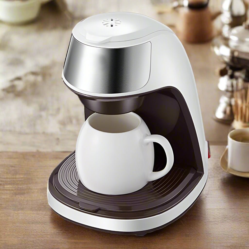 White and silver coffee maker with a white mug on a wooden surface