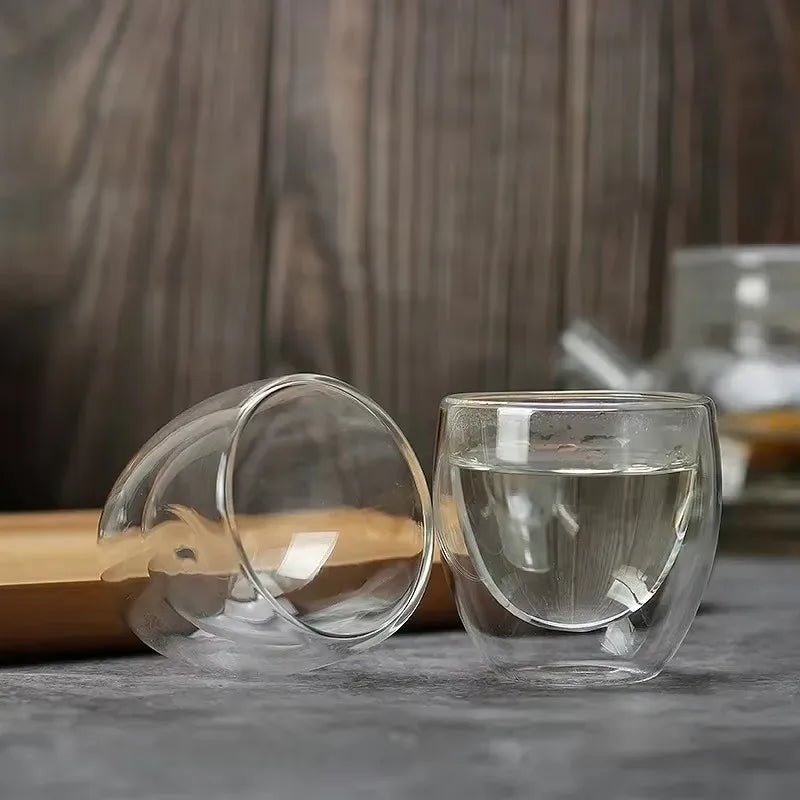 Two clear glass cups with one containing water on a wooden surface.
