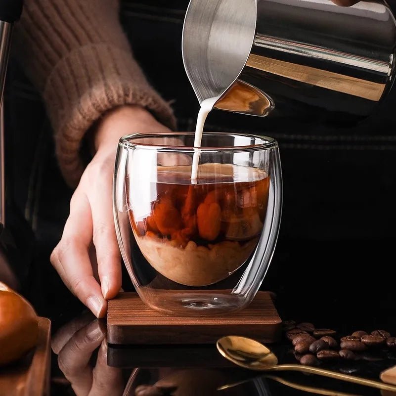 Glass cup with layered dessert being poured into it, surrounded by coffee beans and a spoon.