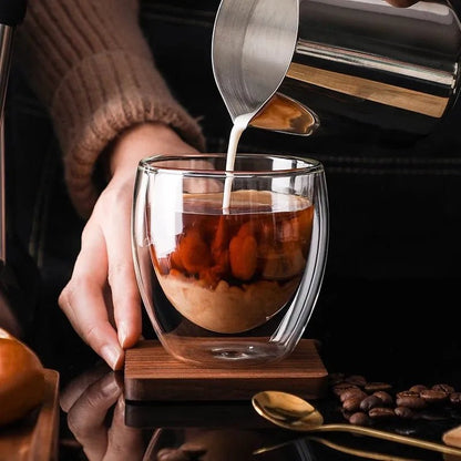 Glass cup with layered dessert being poured into it, surrounded by coffee beans and a spoon.