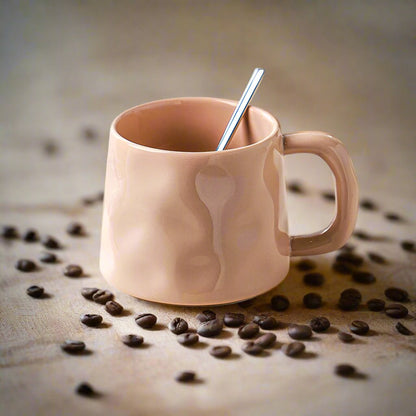 Pink mug with a spoon on a surface surrounded by coffee beans