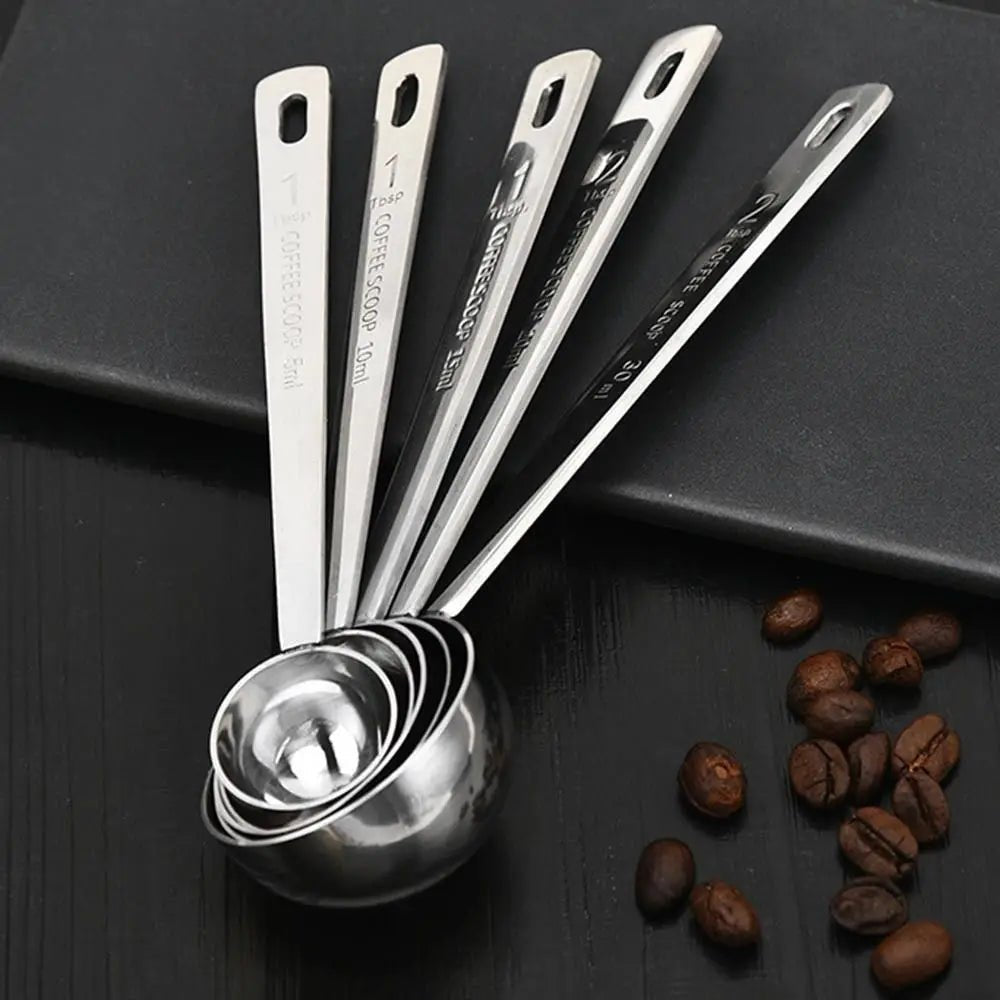 Set of stainless steel measuring spoons on a dark surface with coffee beans.