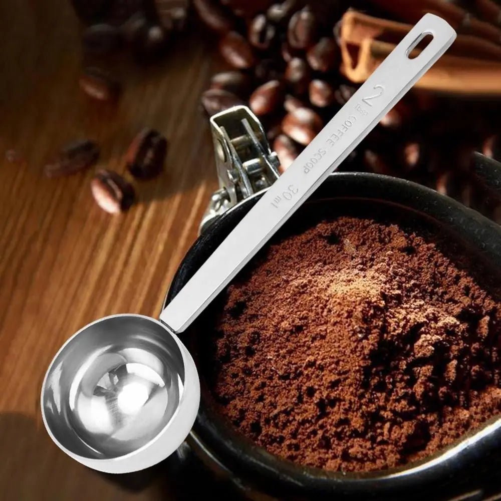 Metal measuring scoop over a bowl of ground coffee with coffee beans in the background