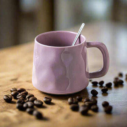 Pink mug with a spoon on a wooden table surrounded by coffee beans