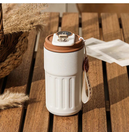 White tumbler with brown lid and handle on a wooden surface