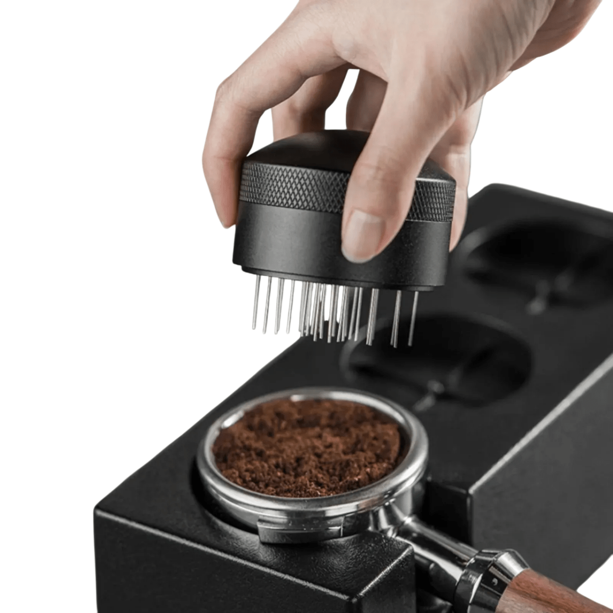 Hand using a coffee grinder to tamp coffee grounds into a portafilter.