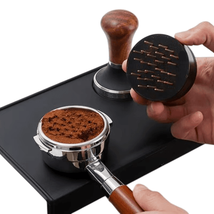 Person using a coffee tamper to compress coffee grounds into a portafilter on a white background.